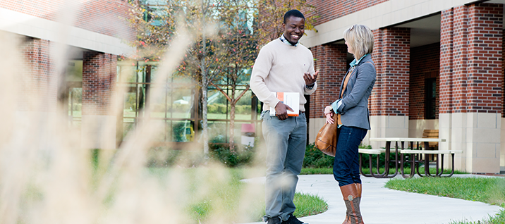 Picture of male and female student talking on campus on sidewalk