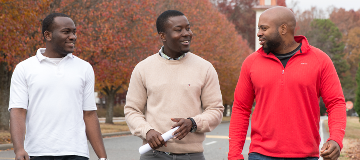 Three African American friends talk together in front of Dallas Campus clock tower