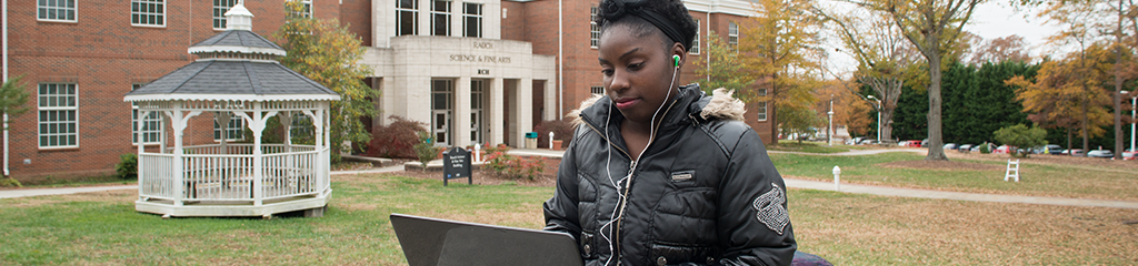 African American female student working on laptop outside on Main Campus