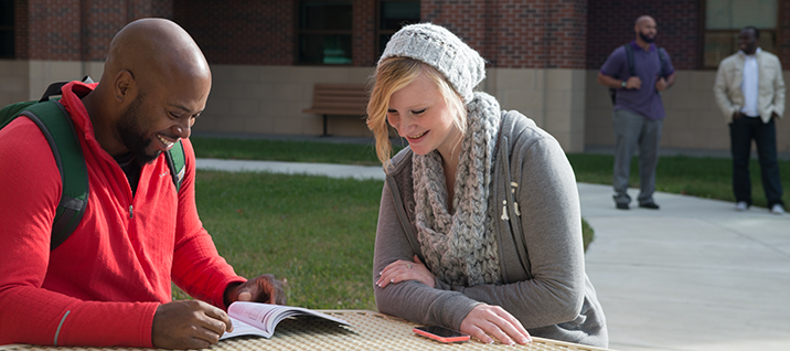 Tow students sit together reading on Dallas Campus