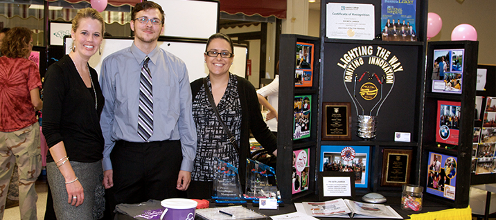 Student proudly stand bext to club booth