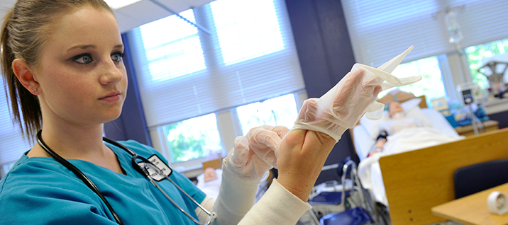 A nursing students pulls a pair of gloves on