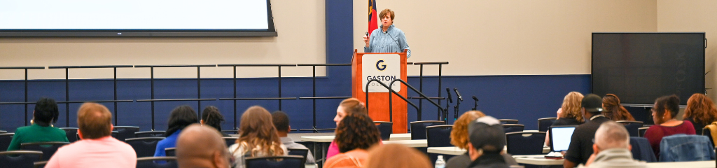 Speaker on a stage at Gaston College with audience members watching.