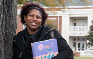 African American female students leans on a tree and smiles at the camera