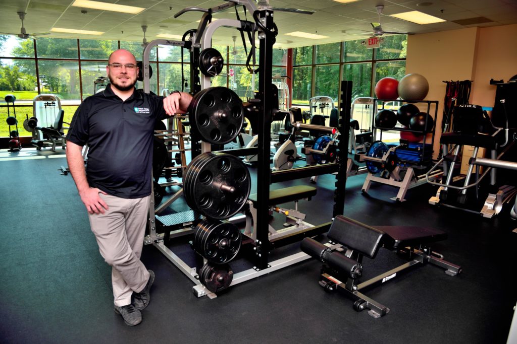 man posing and smiling in gym near exercise equipment