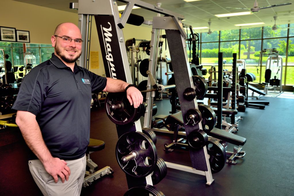 man posing and smiling in gym near exercise equipment