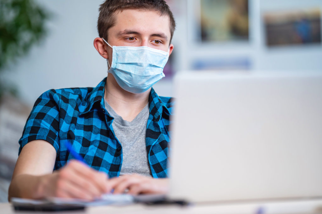 active teenager in mask and headphones with laptop during coronavirus quarantine
