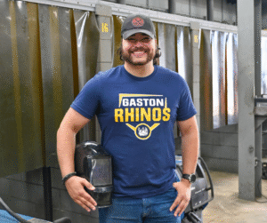 2026 Outstanding Student Lule Balbosa, Smiling man with beard wearing blue Gaston Rhinos t-shirt and baseball cap.