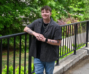 2026 Gaston College Dallas Herring Award Winner Alycia Evans - smiling, wearing dark shirt, standing at fence on campus.