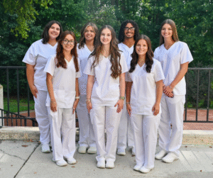 Group photo of 7 nursing student graduates outside wearing white scrubs